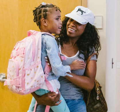 mother picking up young child from school - holding her in her arms